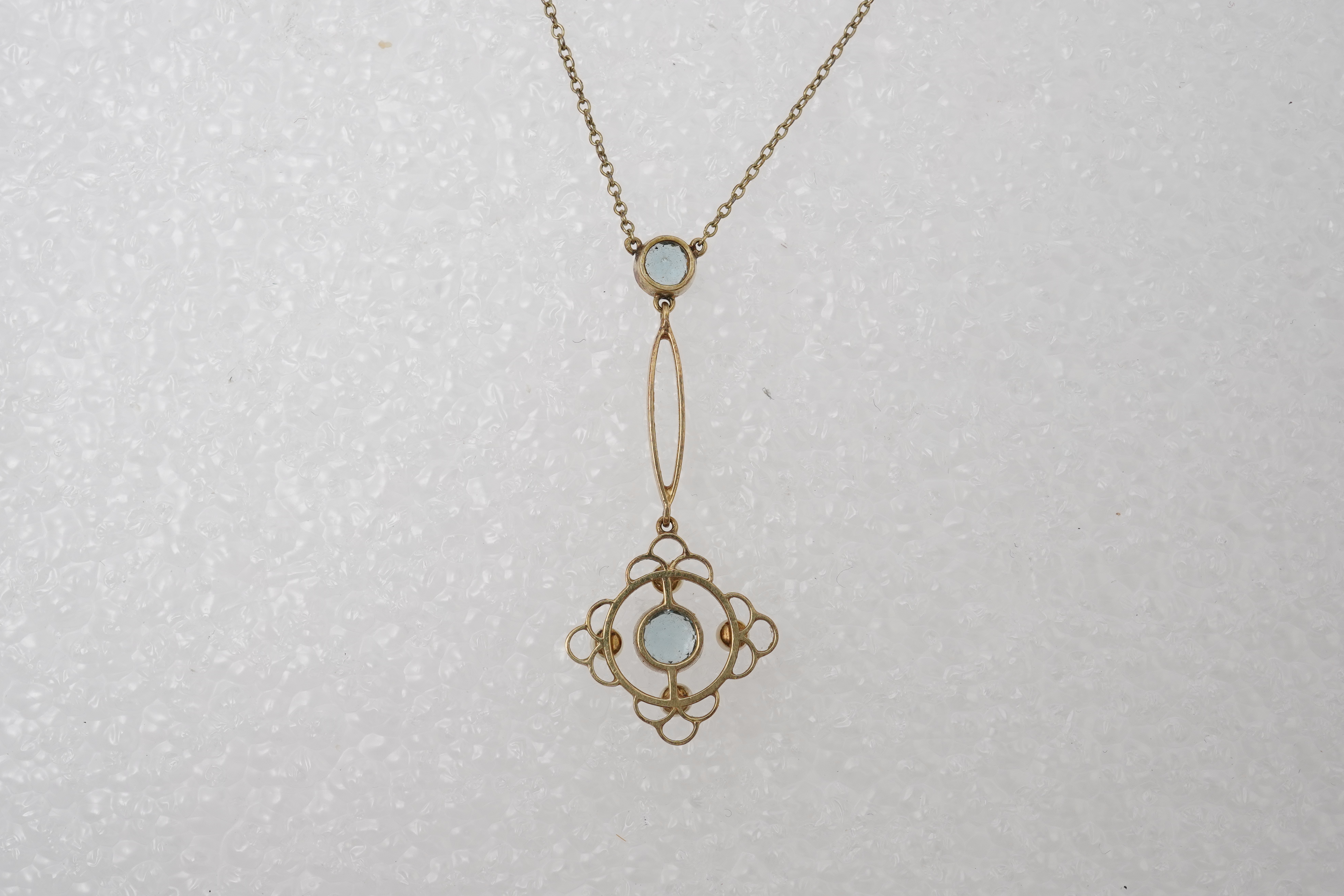 An Edwardian circular-cut aquamarine and seed pearl pendant, early 20th century, of foliate design, mounted in gold, pendant length 4cm, chain length 40cm, clasp stamped 15, gross weight approximately 3 grams, pearls unt